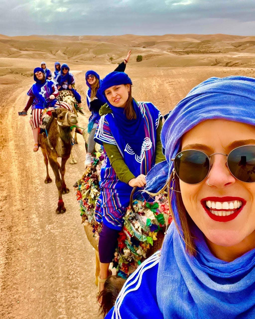 Selfie with woman in blue headwrap and camel caravan behind