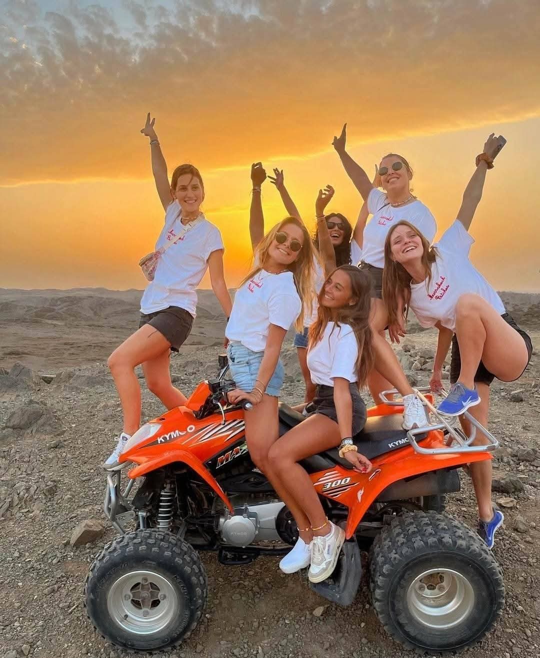 Group of young women celebrating on orange ATVs at golden sunset