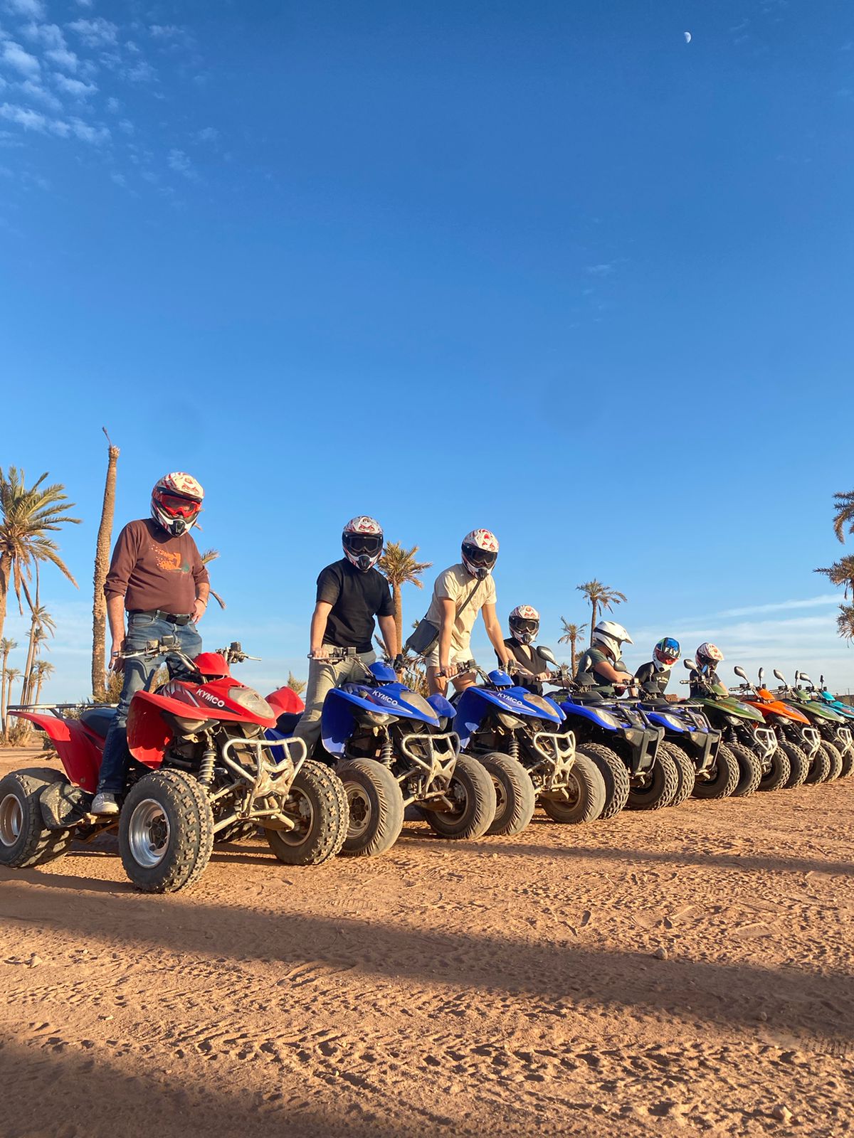 Large group of people with colorful ATVs lined up in desert with palm trees