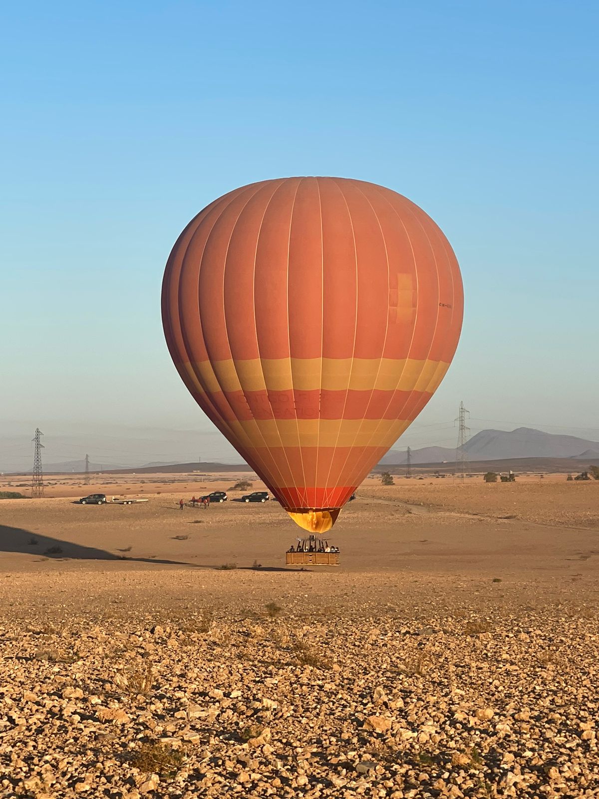Single orange hot air balloon landed in desert landscape
