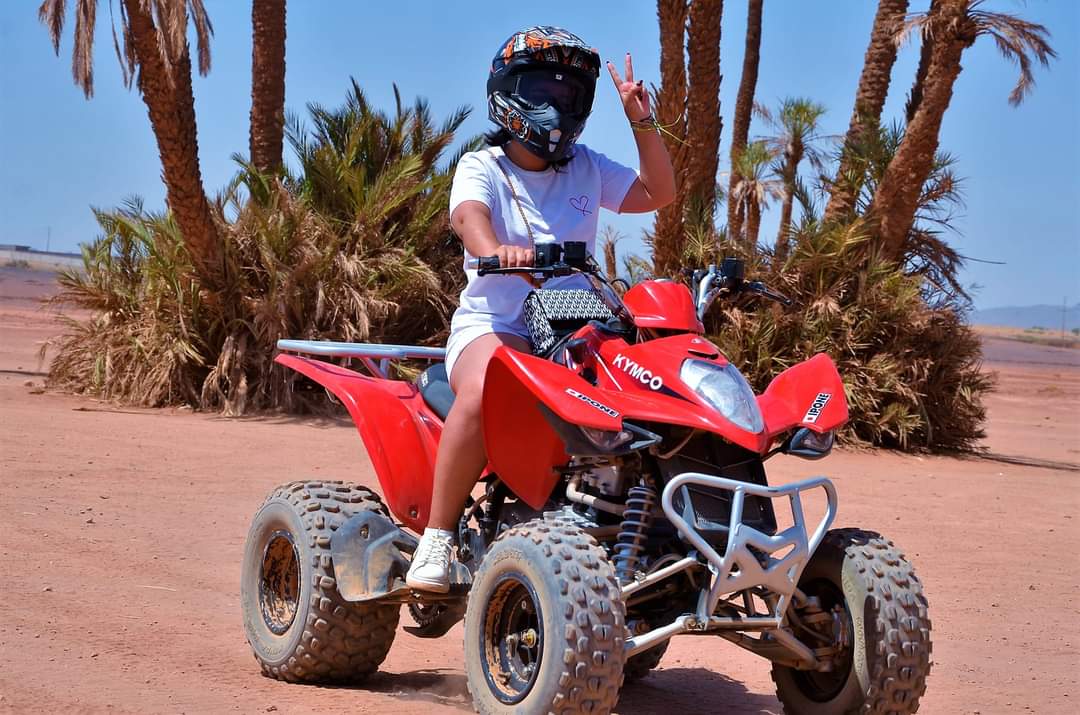 Person making peace sign on red Kymco ATV among palm trees