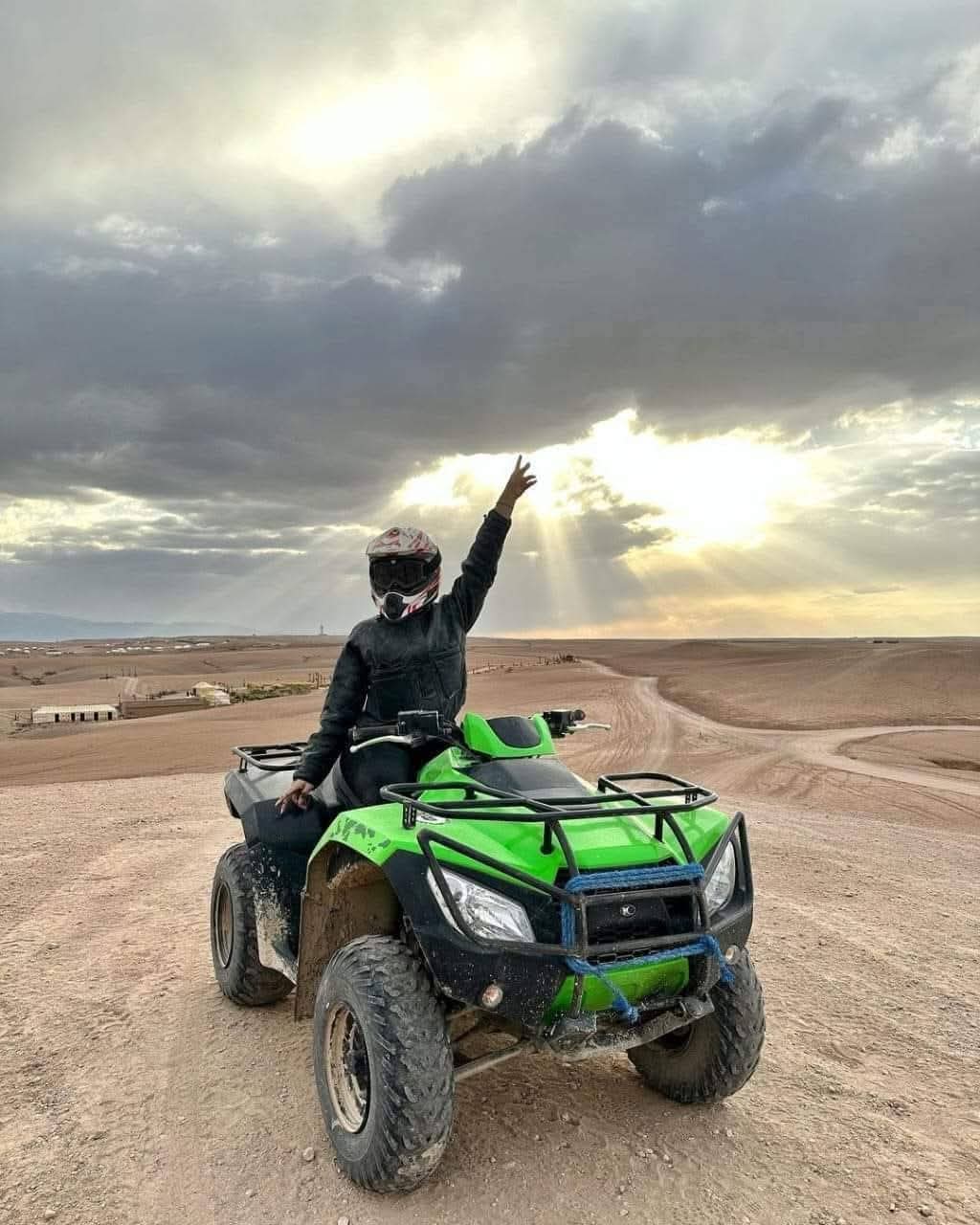 Rider on green quad with arms raised at dramatic sunset