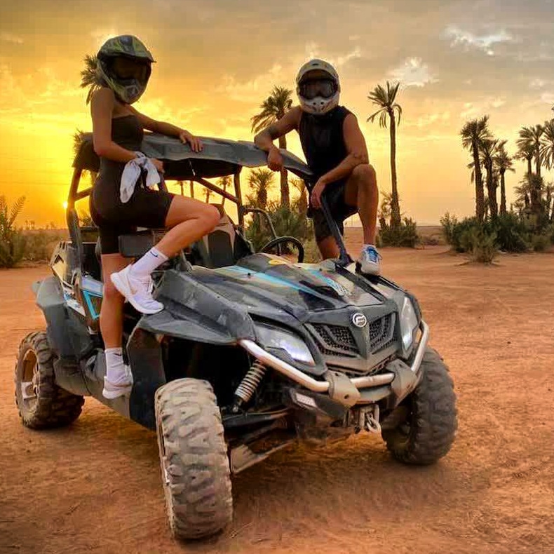 Two women posing on buggy at sunset among palm trees