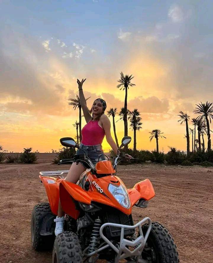 Woman celebrating on orange ATV at sunset with palm trees