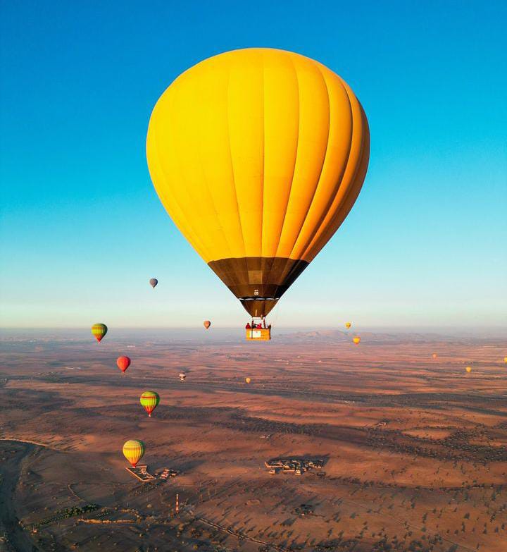 Aerial view of yellow hot air balloon with multiple colorful balloons over desert